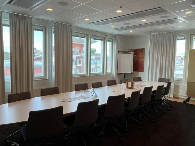 Ett konferensrum med ett långt bord, flera stolar och fönster som släpper in naturligt ljus.