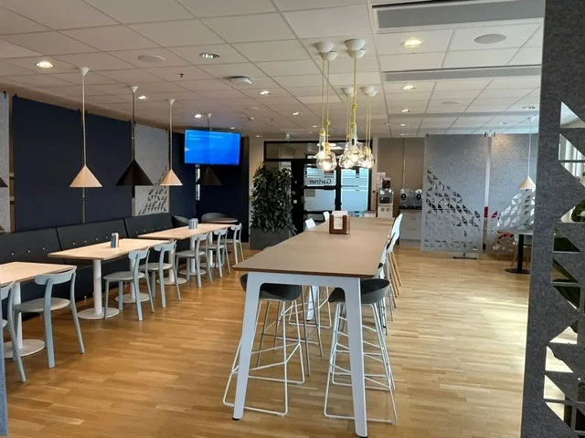 Ett rymligt matsalsområde med höga bord, stolar, taklampor och en TV på väggen.