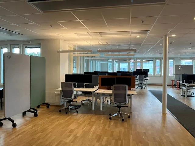 En arbetsyta med skrivbord, stolar och datorer i ett öppet kontorsområde.