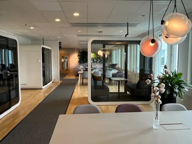 Ett modernt kontor med bord, stolar, glasväggar och hängande lampor.