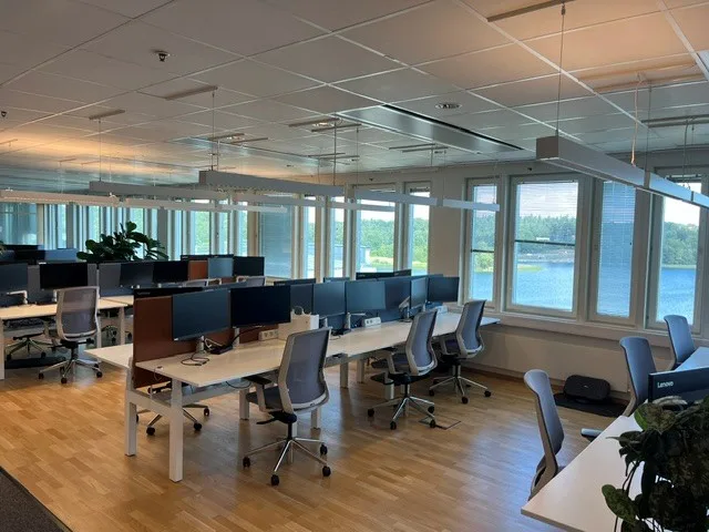 Flera arbetsstationer med skrivbord och stolar vid fönster som vetter mot en sjö.
