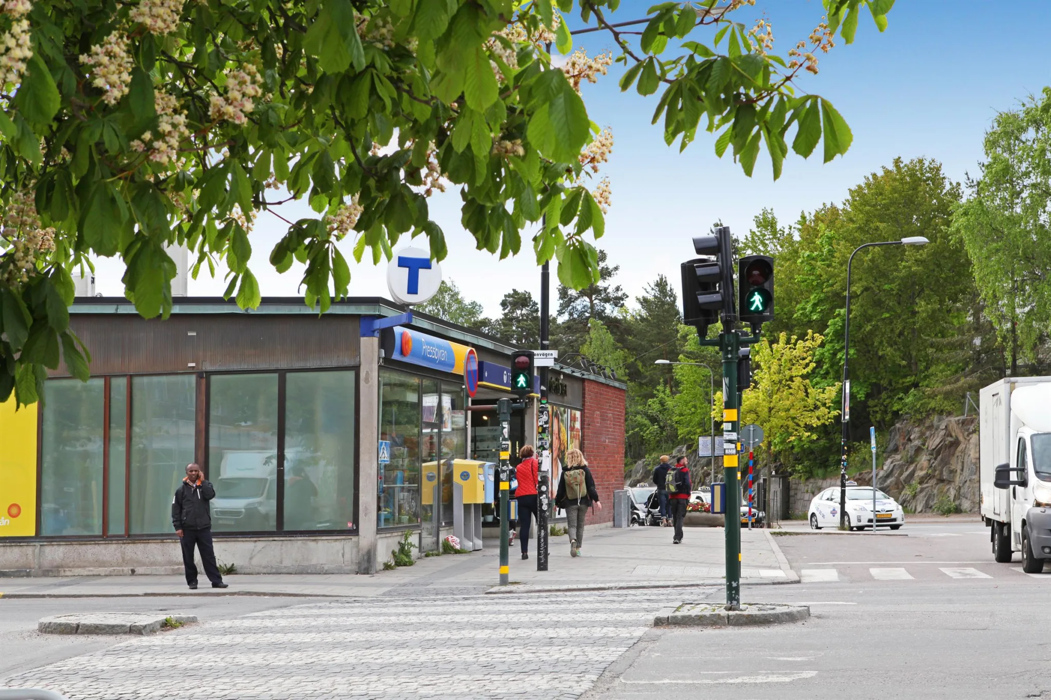 4. En trottoar framför en tunnelbanestation, med människor som går och trafikljus som visar grönt.