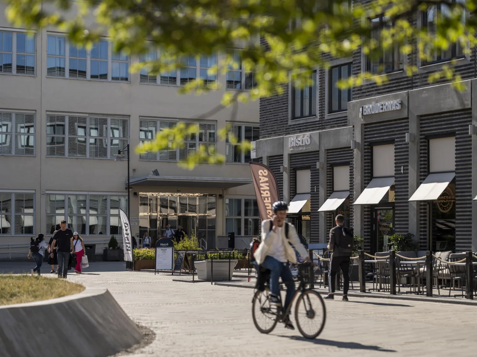 En person cyklar på en innergård omgiven av byggnader med butiker och caféer.