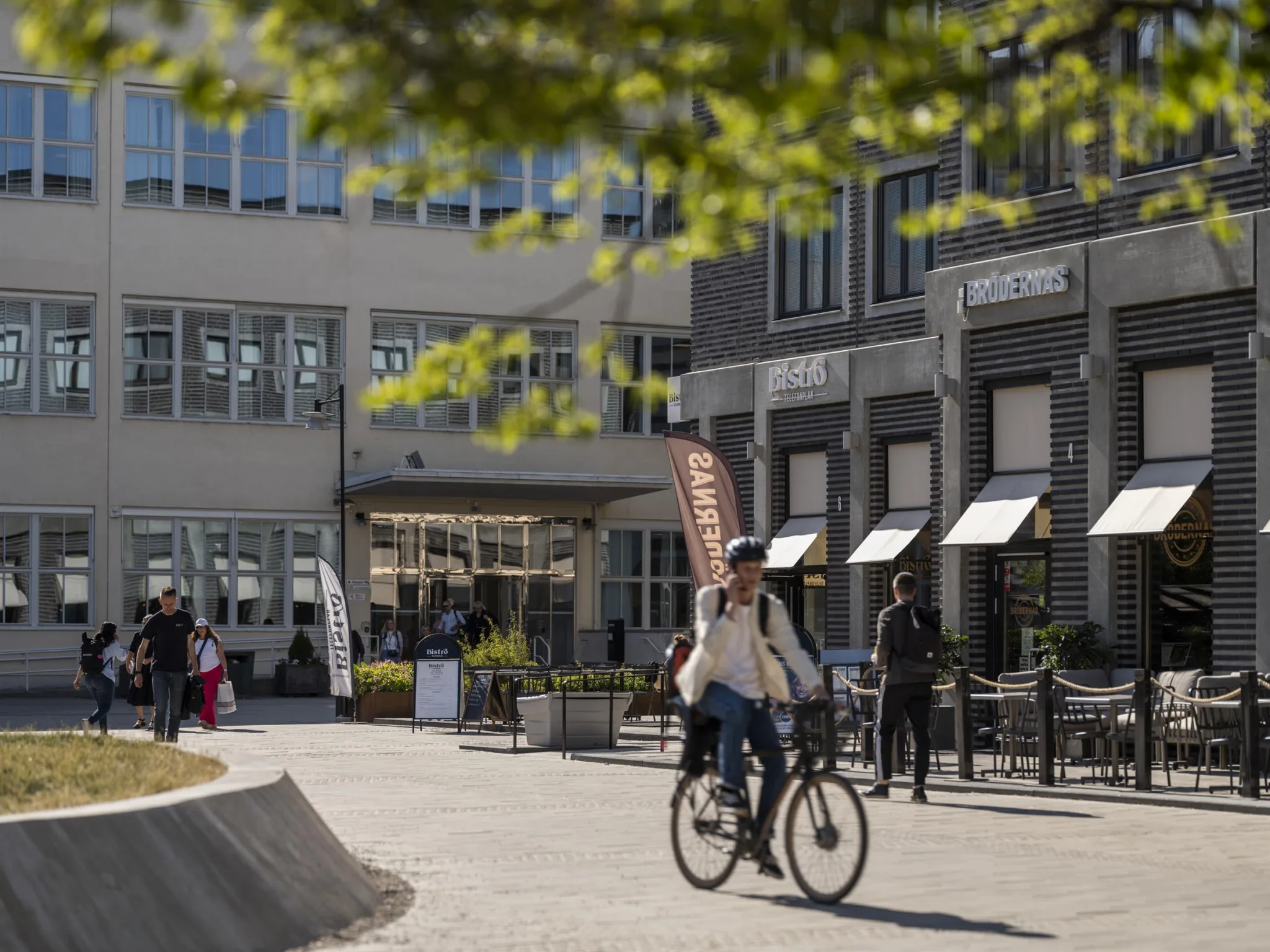 En person cyklar på en innergård omgiven av byggnader med butiker och caféer.