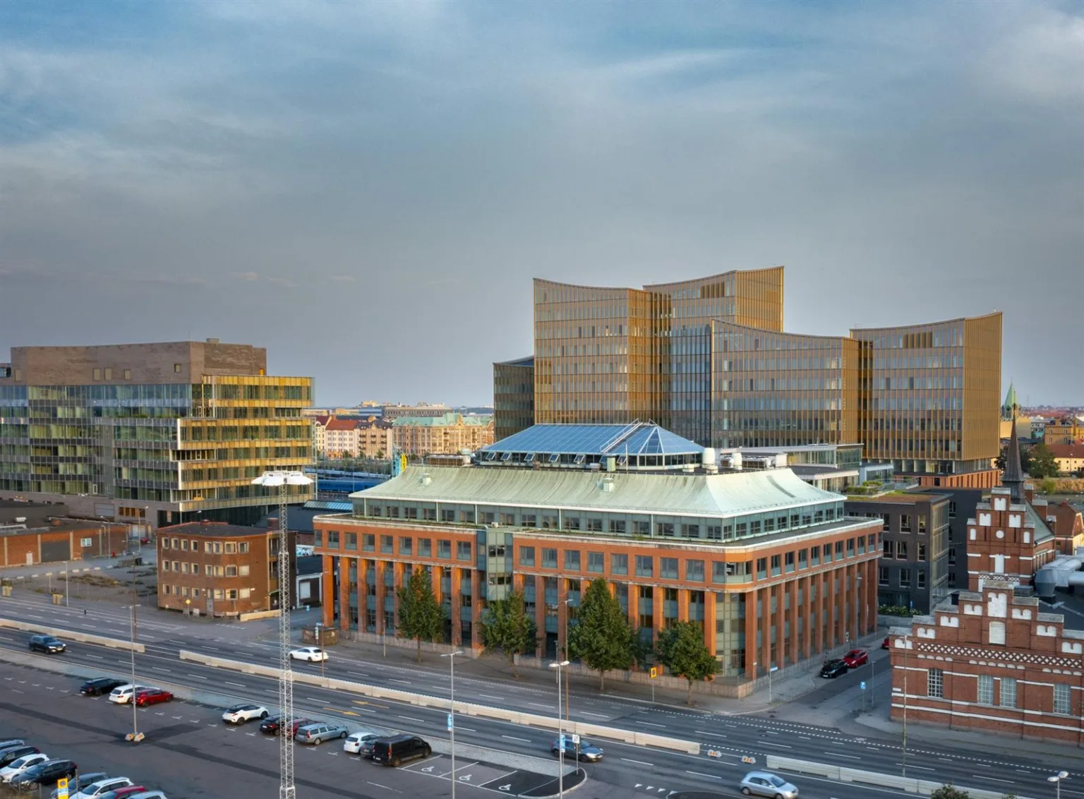 5. Vy över stadsmiljö med en större tegelbyggnad med glasdetaljer och moderna kontorsbyggnader i bakgrunden.