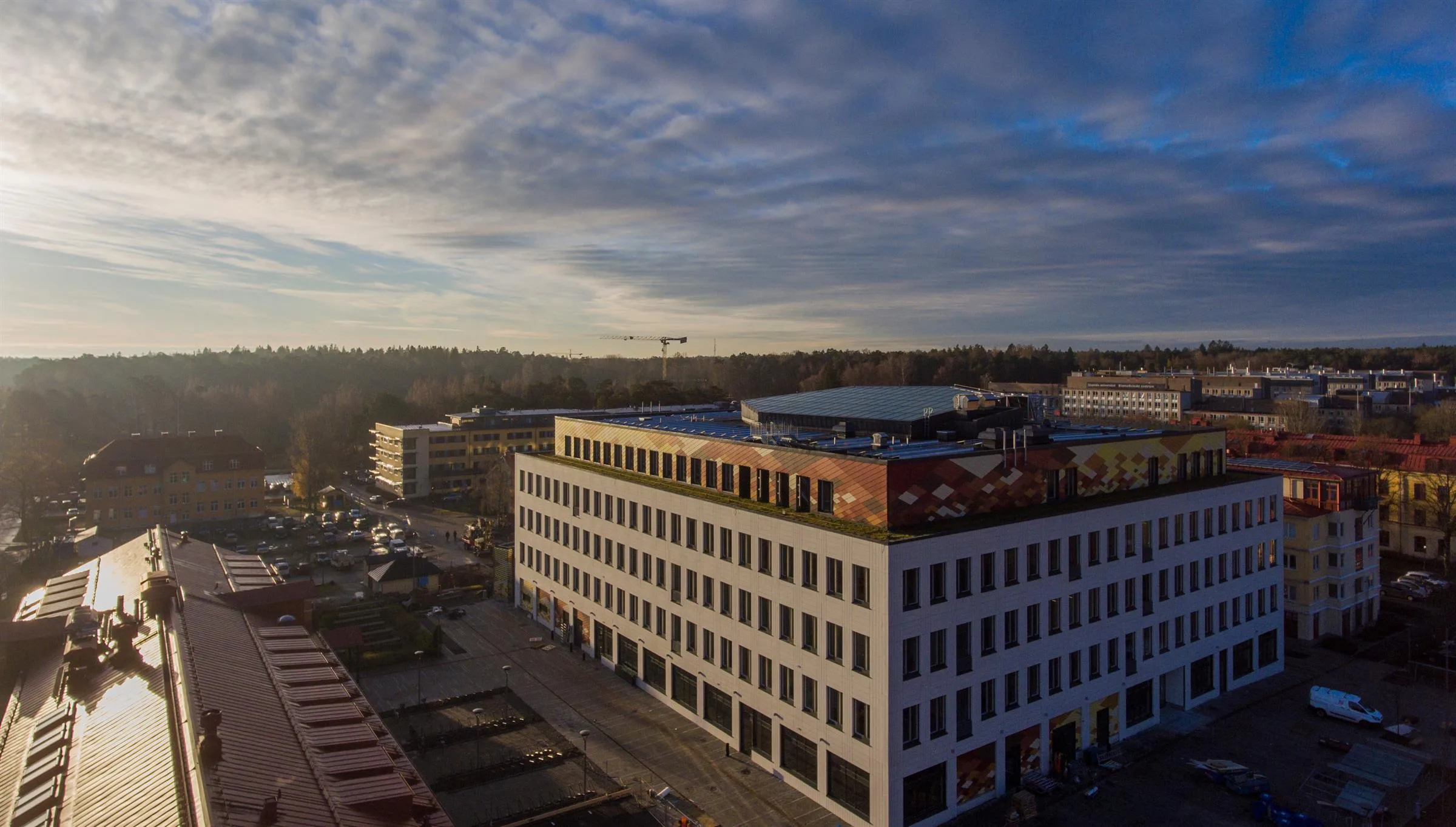 En rektangulär byggnad med vit fasad och stora fönster, omgiven av grönska under en himmel med spridda moln.