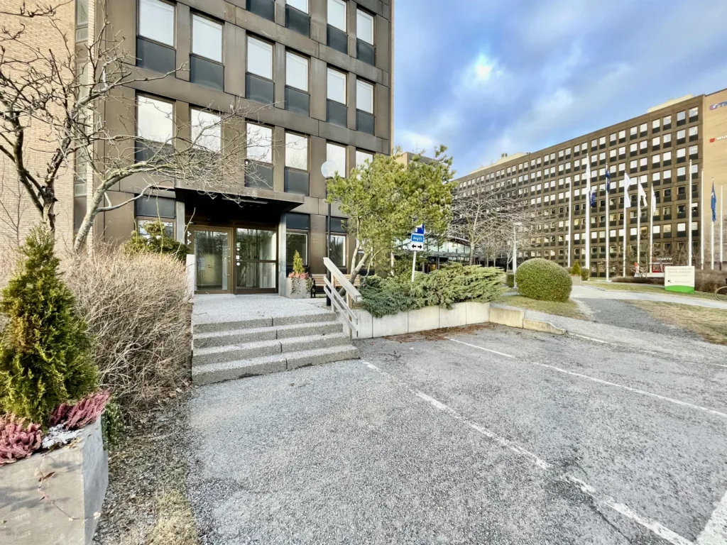 Bostadsbyggnad med en trappa och en entré omgiven av grönska.