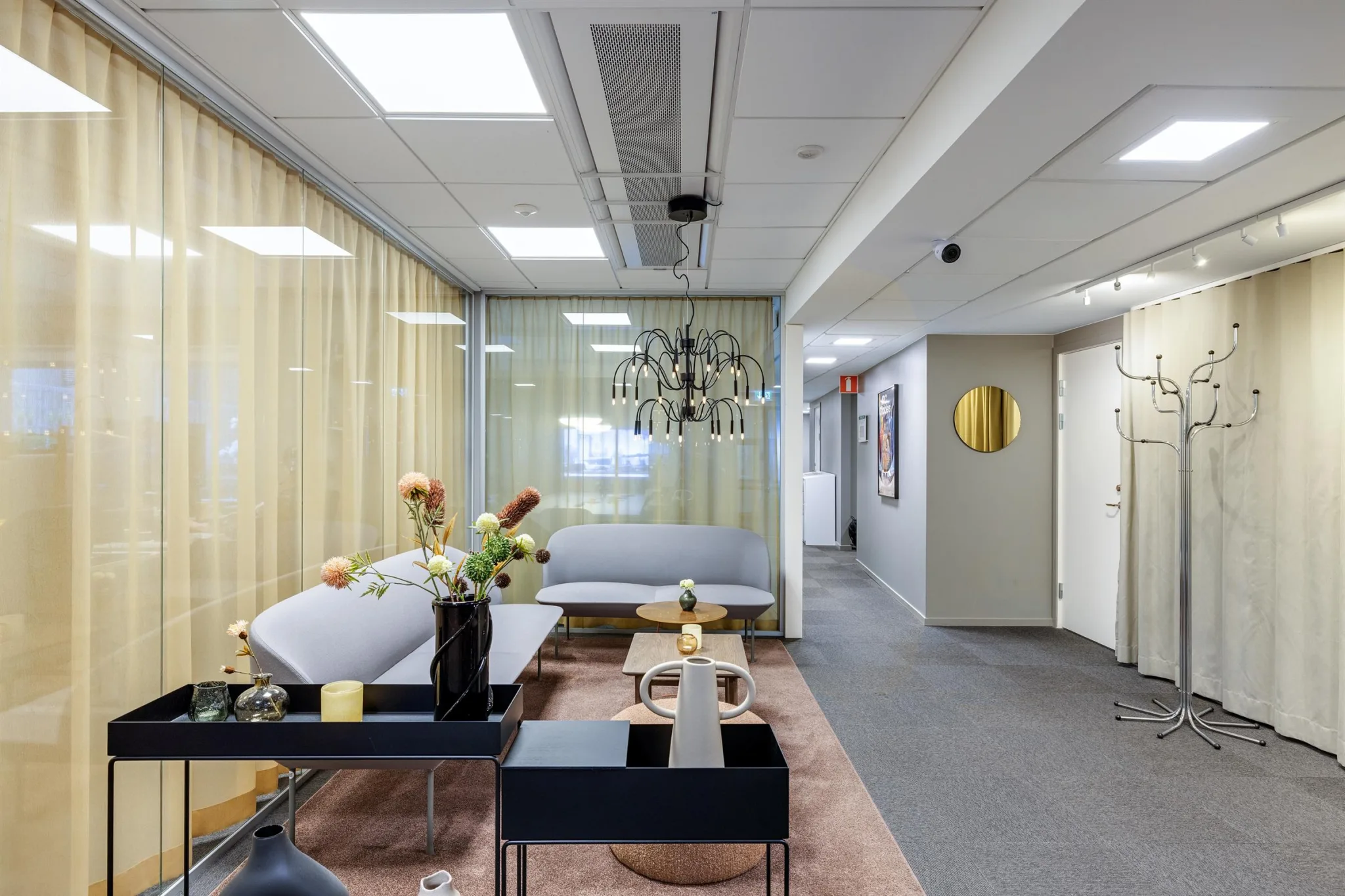 En lounge med soffor, ett bord, blommor och en dekorativ taklampa.