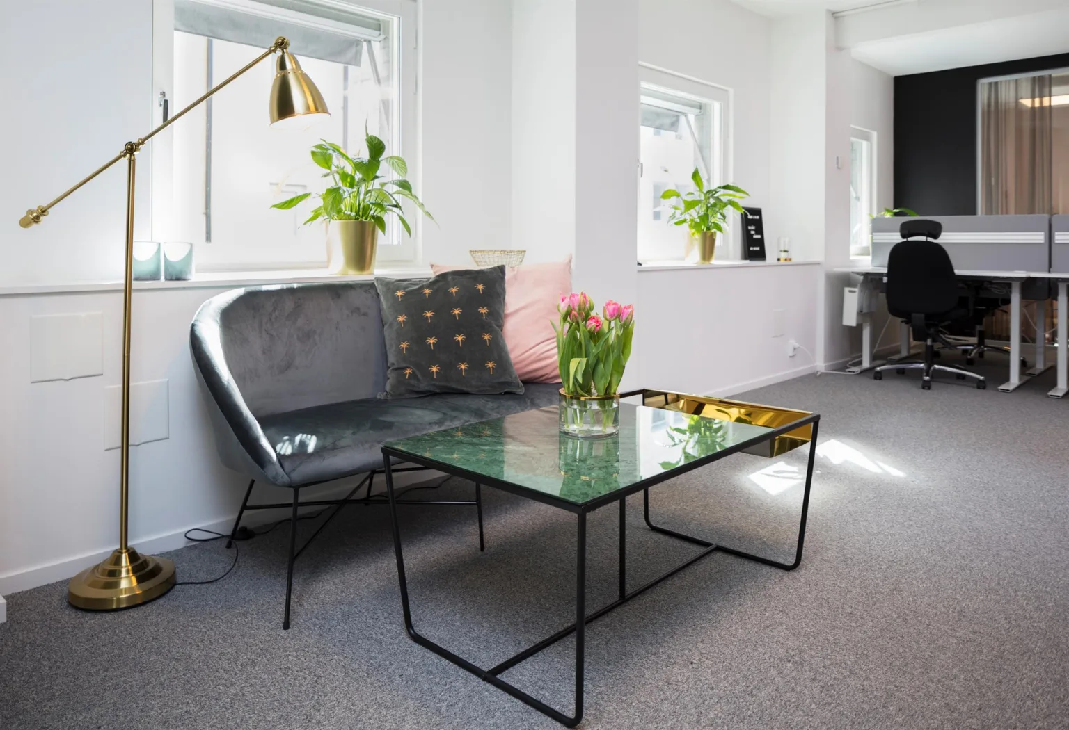 3. Grå soffa och glasbord med rosa tulpaner, omgivna av växter i ett ljust rum.