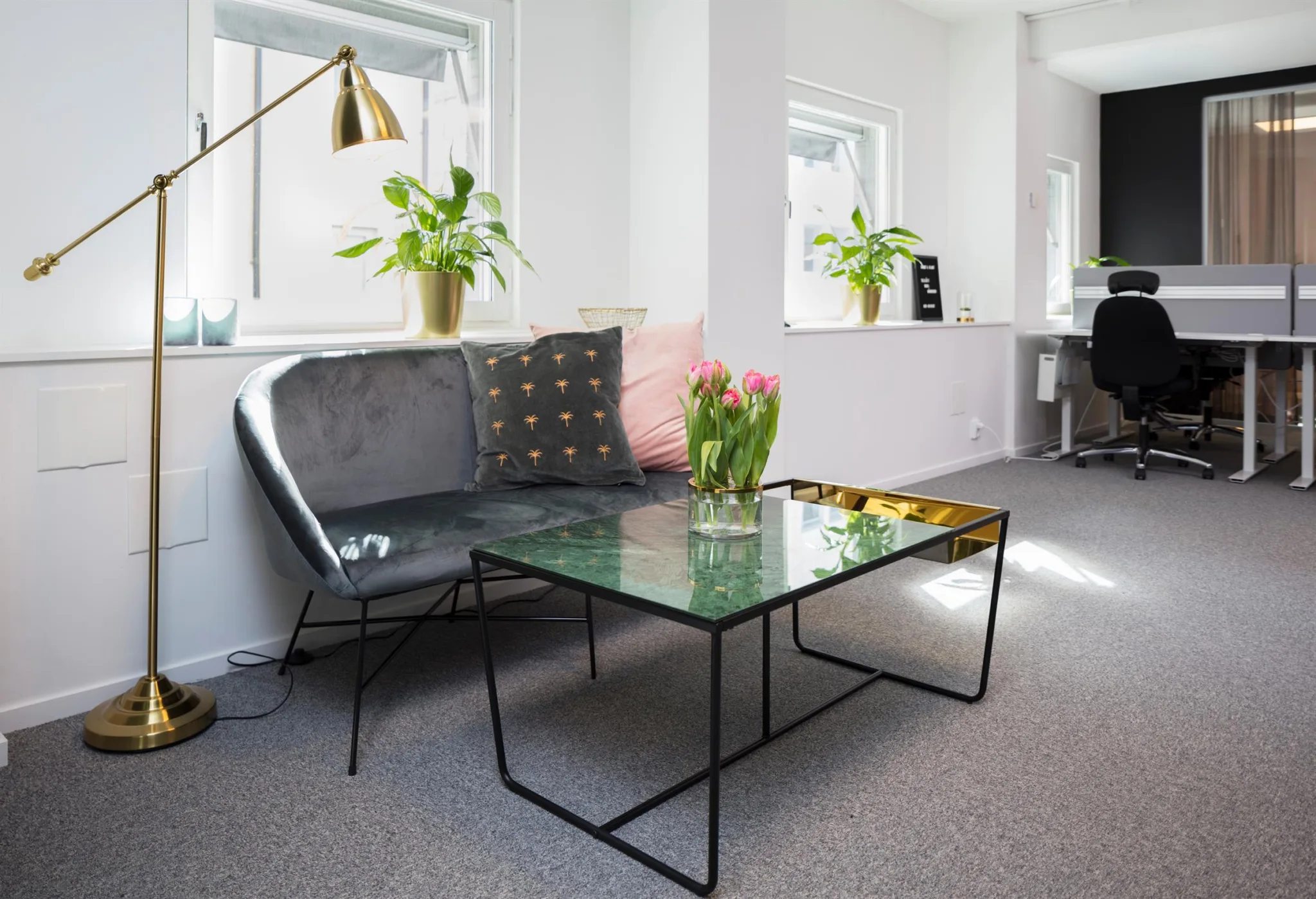 3. Grå soffa och glasbord med rosa tulpaner, omgivna av växter i ett ljust rum.