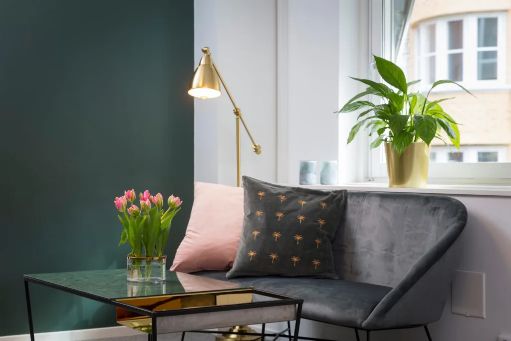 2. Ett vardagsrum med en grå soffa, färgglada kuddar, en guldlampa och en vas med rosa tulpaner.