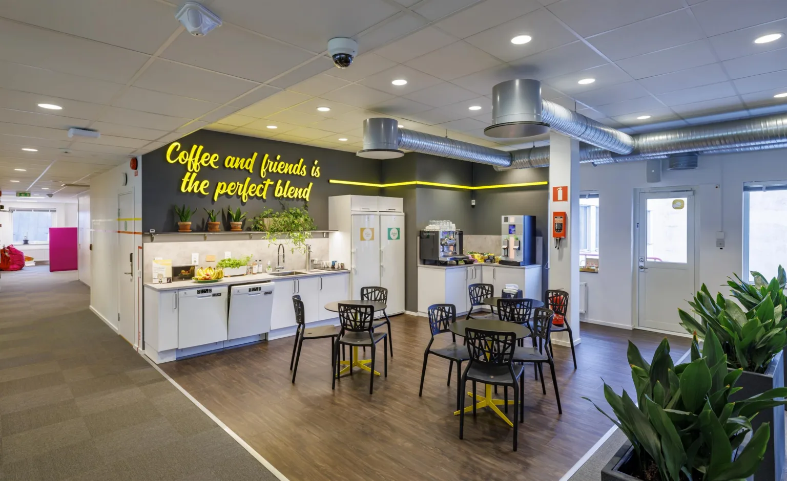 1. Ett modernt fikarum med bord, stolar och texten "Coffee and friends is the perfect blend" på väggen.