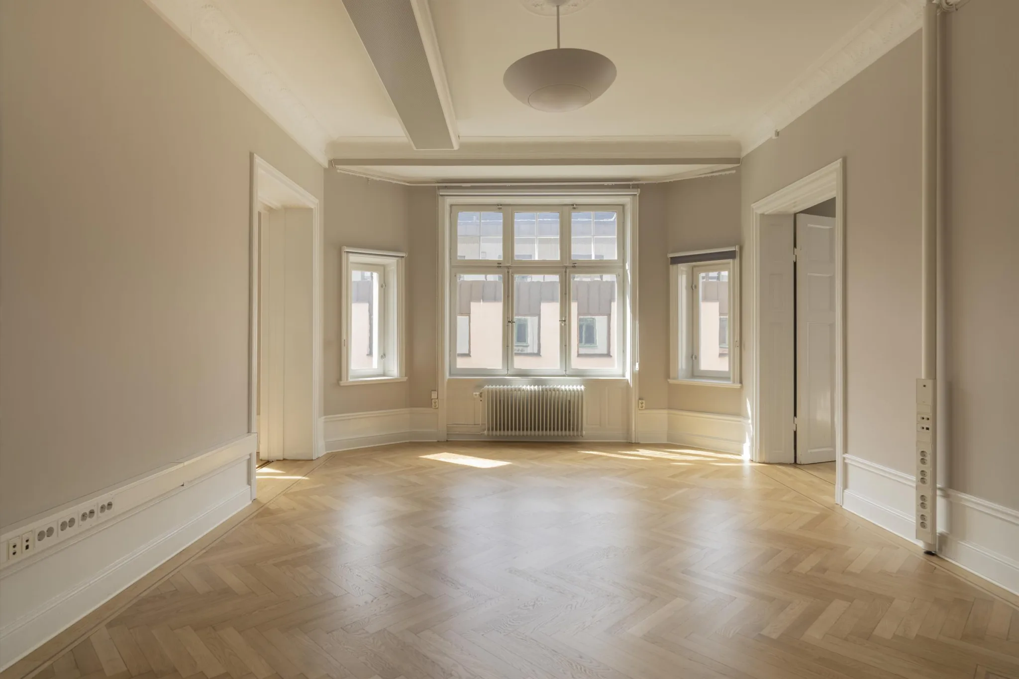 4. Ljust rum med parkettgolv och flera fönster, inklusive ett större fönster med radiator under.