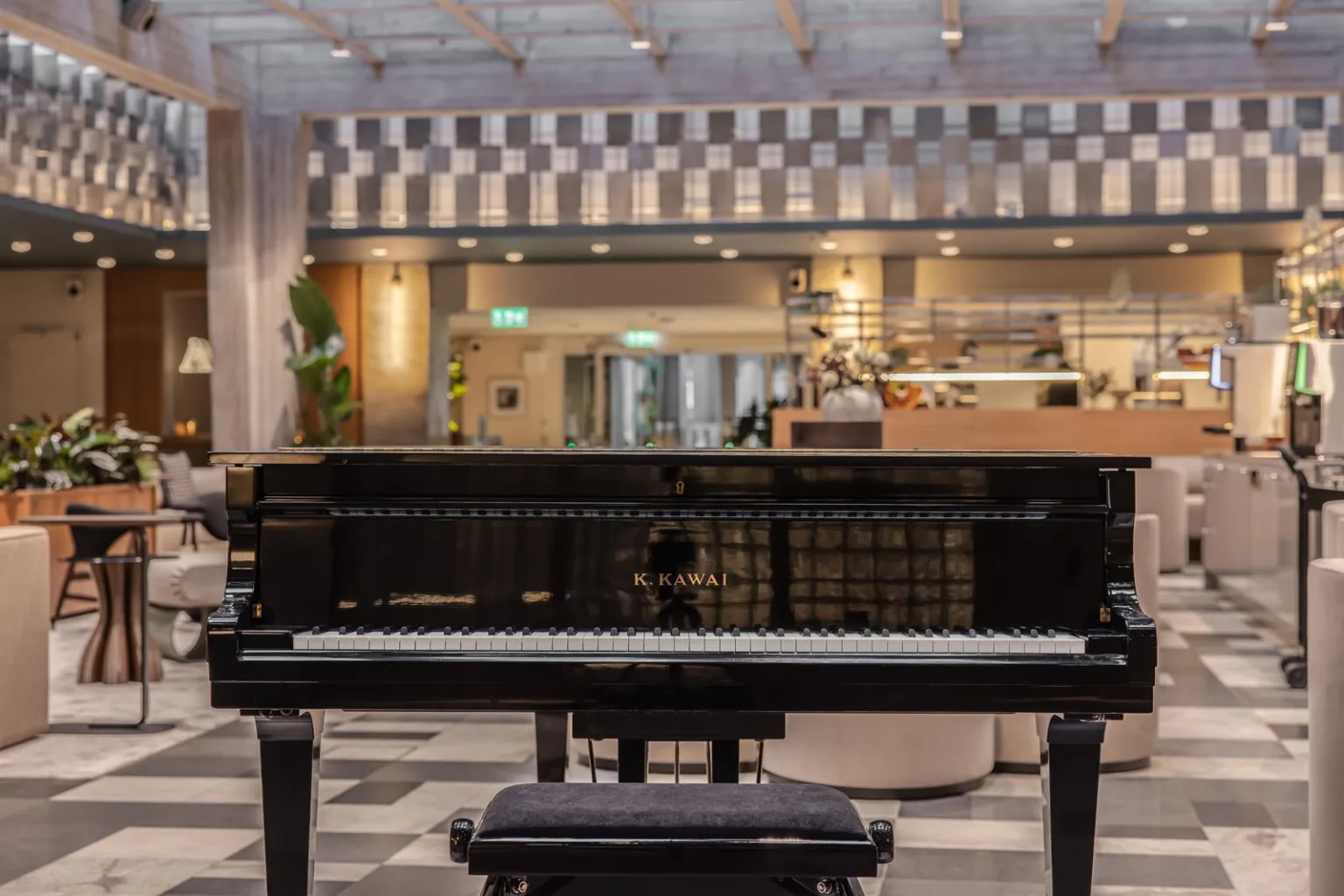 En svart flygel står i centrum av en rymlig lokal med rutigt golv och en kafédisk i bakgrunden.