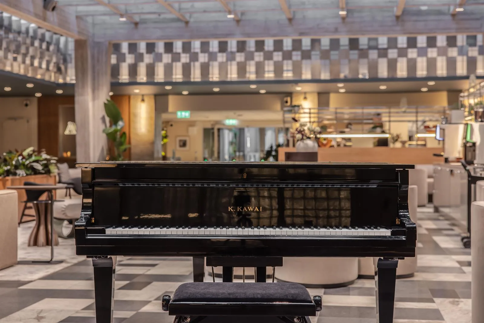 En svart flygel står i centrum av en rymlig lokal med rutigt golv och en kafédisk i bakgrunden.