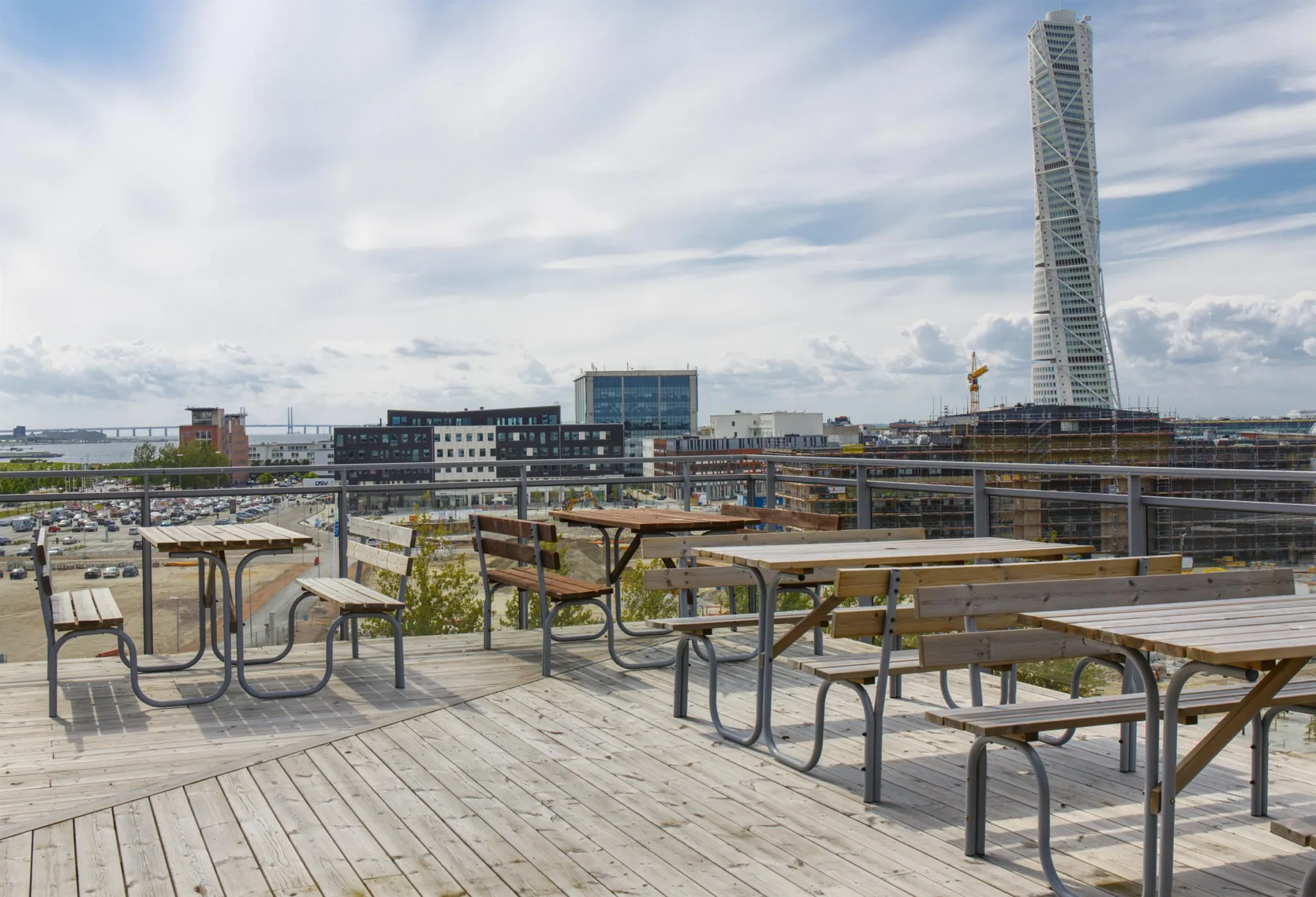 1. Flera träbord och bänkar står på en takterrass med utsikt över staden och Turning Torso i bakgrunden.