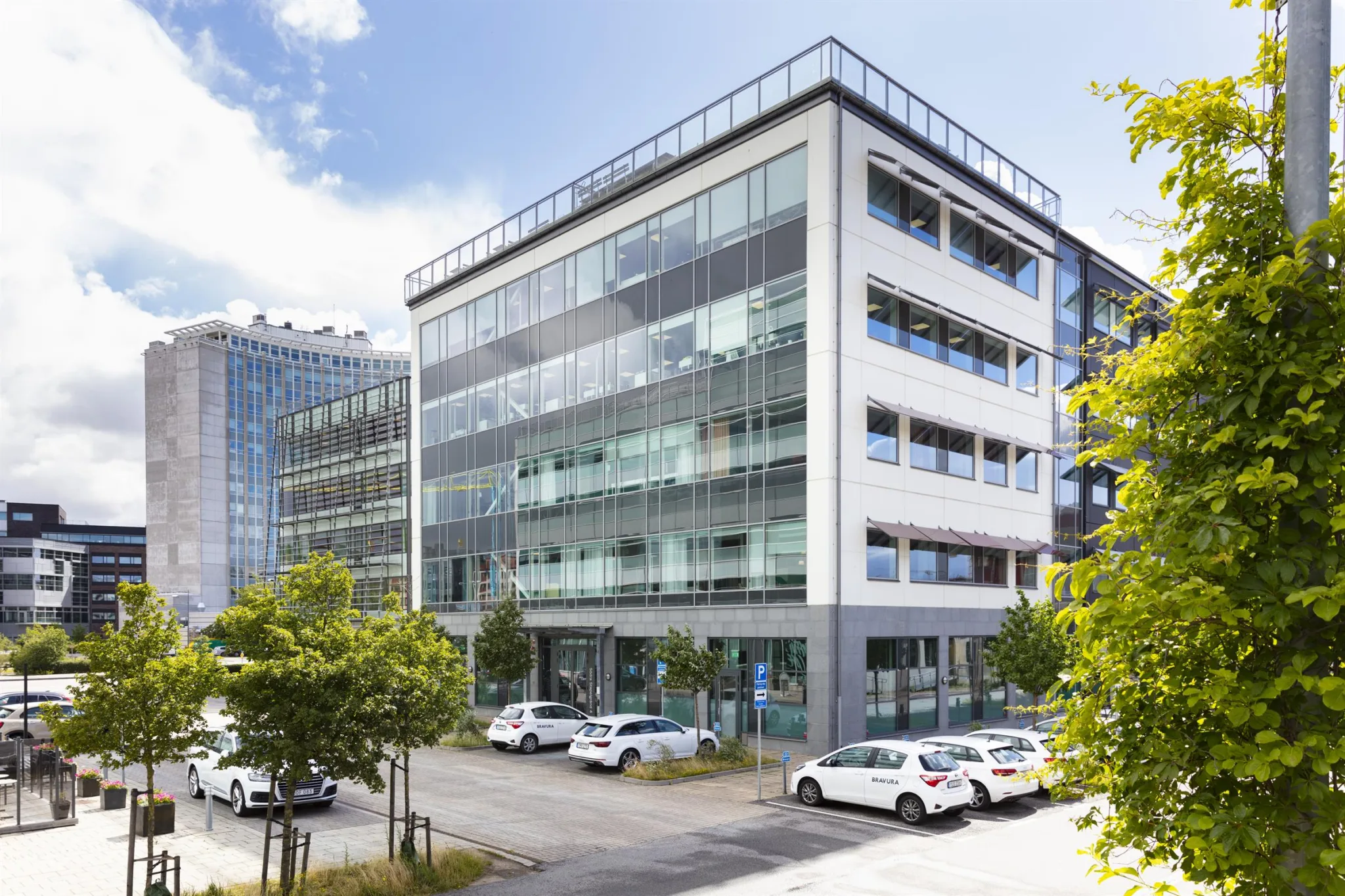 4. En modern kontorsbyggnad i glas och metall med parkerade bilar framför och träd runtomkring.