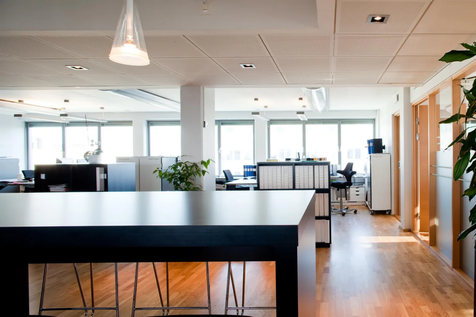 Ett luftigt kontor med skrivbord, stolar, förvaringsskåp och stora fönster som släpper in naturligt ljus.