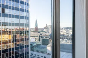 Utsikt genom ett fönster mot stadens byggnader och en kyrkspira.