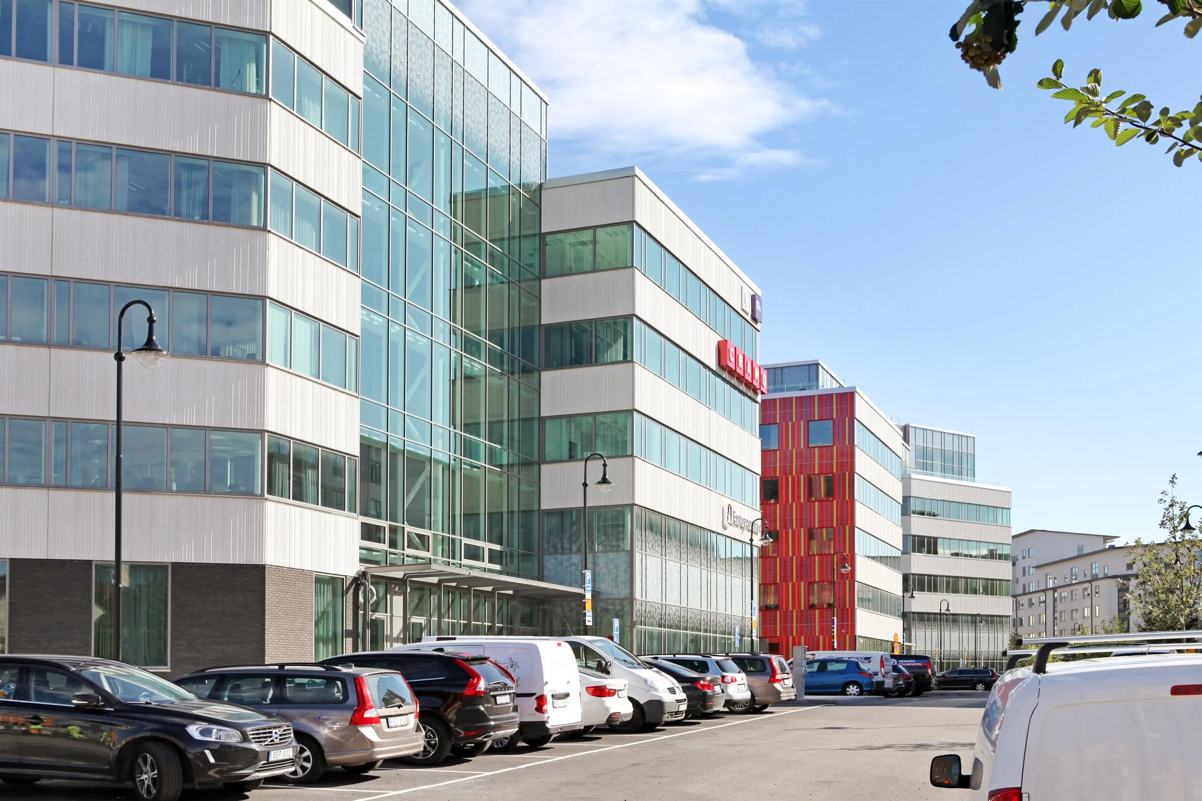 En rad moderna kontorsbyggnader med glas och betongfasader, parkerade bilar längs gatan.